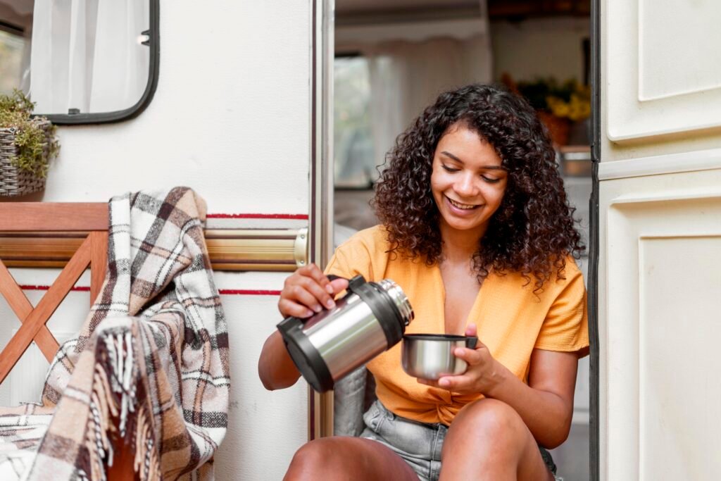 Woman holding flask and flask cover attempting to pour in flask coffee - having coffee at home