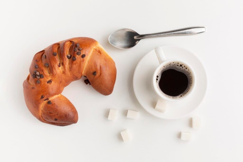 Coffee and bagal on a white surface with a tea spoon and sugar
