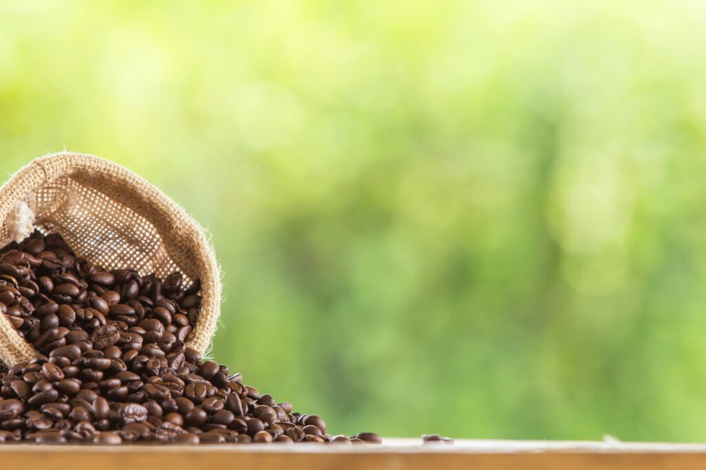 Coffee beans in a sack on wooden tabletop against grunge green blur background