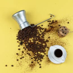 flat lay coffee beans in jug with glass jar, cup of coffee, chocolate chip cookies on yellow background. horizontal